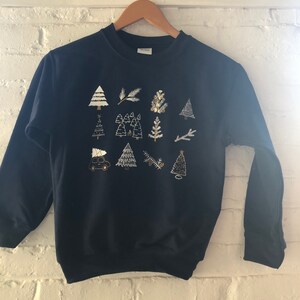 May include: A navy blue sweatshirt with a gold and white design of Christmas trees, branches, and a car carrying a Christmas tree.