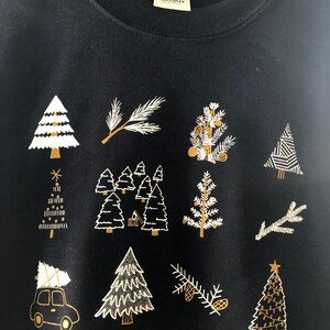 May include: Black sweatshirt with a gold and white Christmas tree design. The design features multiple trees, branches, and pine cones.