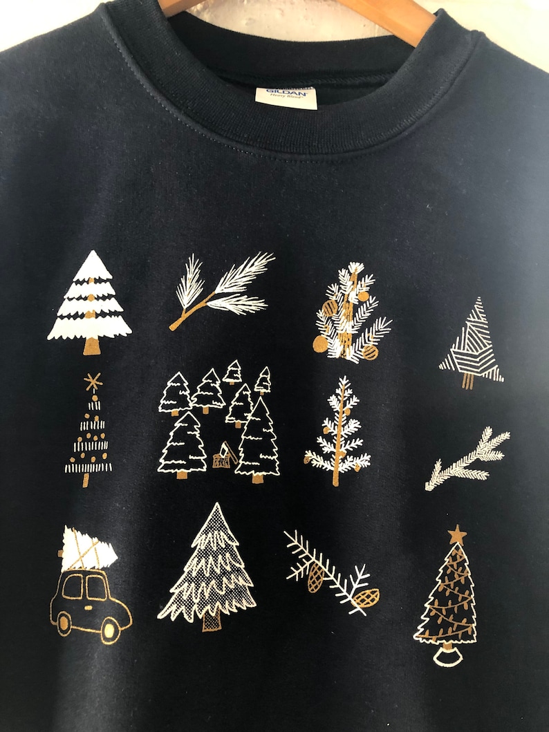May include: Black sweatshirt with a gold and white Christmas tree design. The design features multiple trees, branches, and pine cones.