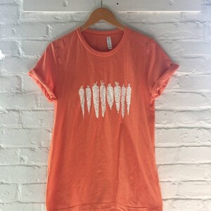 May include: A coral orange t-shirt with a white graphic of a row of carrots.