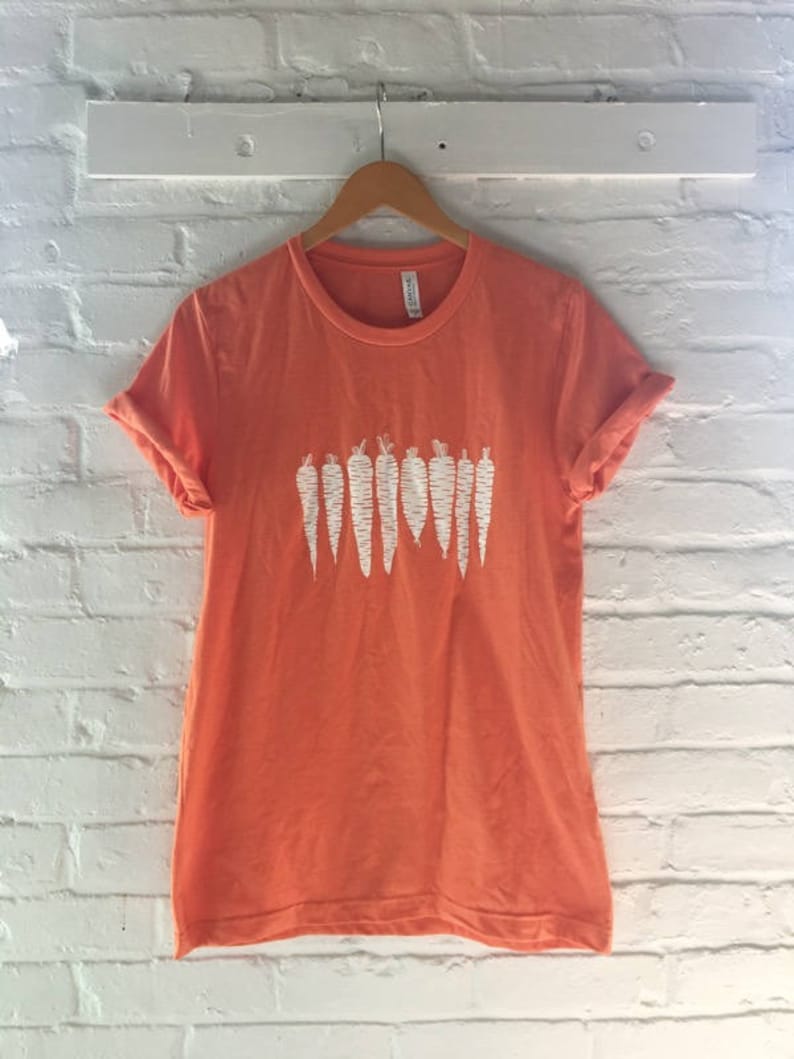 May include: A coral orange t-shirt with a white graphic of a row of carrots.