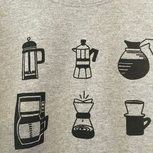 May include: A grey sweatshirt with six black illustrations of different coffee brewing methods: a French press, a Moka pot, a drip coffee maker, a pour-over coffee maker, a percolator, and a Chemex.