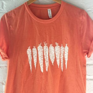 May include: Orange t-shirt with a white graphic of a row of carrots.