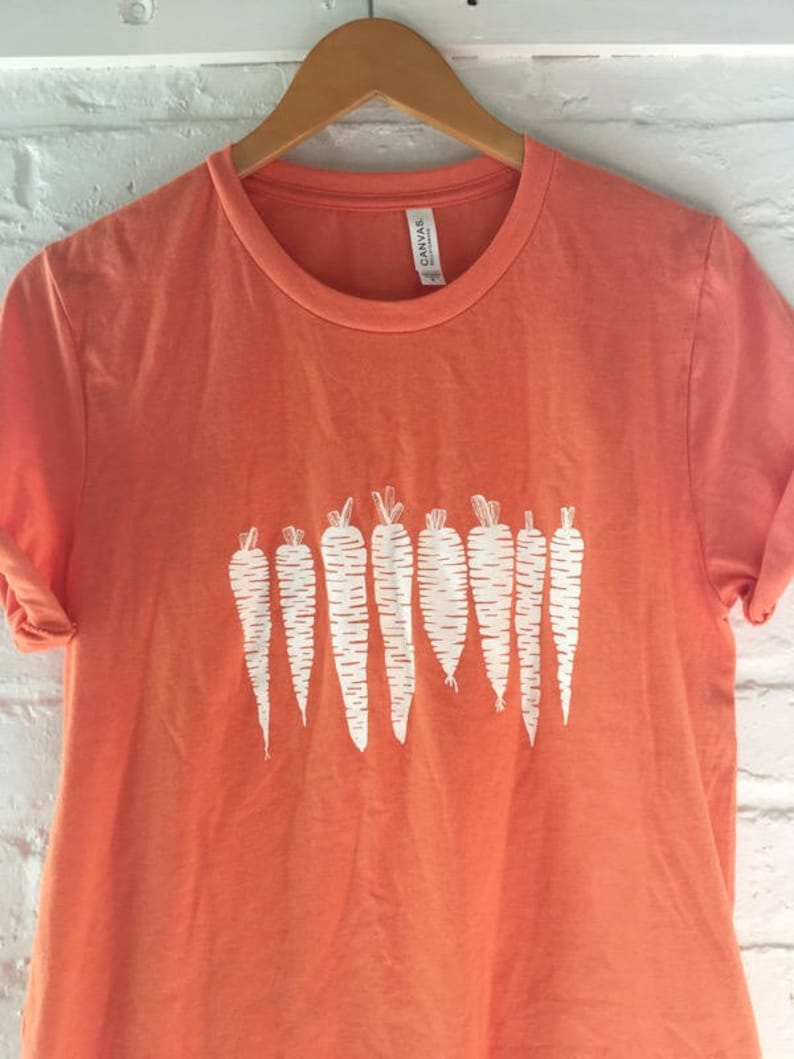 May include: Orange t-shirt with a white graphic of a row of carrots.