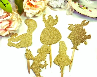 May include: Six gold glitter cupcake toppers featuring characters from Alice in Wonderland. The characters include the Mad Hatter, the Queen of Hearts, the Cheshire Cat, Alice, and the White Rabbit.
