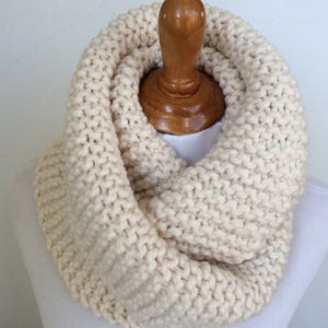 May include: A cream-colored knitted infinity scarf, displayed on a wooden mannequin.