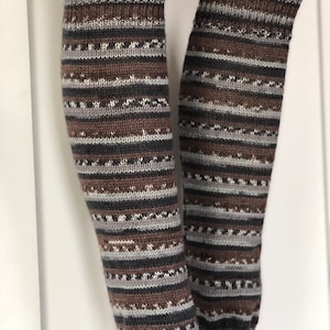 May include: A pair of brown, gray, and white striped leg warmers. The leg warmers are knitted and have a textured pattern.