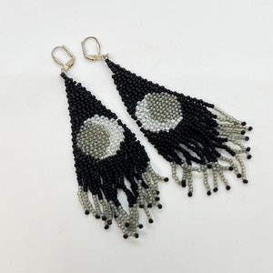 May include: A pair of long, black and silver beaded earrings with a fringe design. The earrings feature a circular pattern of silver beads in the center.