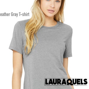 Puede incluir: Una camiseta gris jaspeado con mangas cortas y cuello redondo. La camiseta est&aacute; hecha de un material suave y c&oacute;modo. El texto "Heather Gray T-shirt" se muestra en la parte superior izquierda de la imagen. El nombre de la marca "LAURAQUELS" se muestra en la parte inferior derecha.
