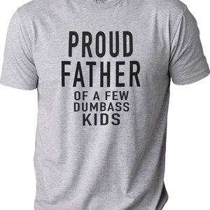 Puede incluir: Camiseta gris jaspeado con el texto "PROUD FATHER OF A FEW DUMBASS KIDS" en letras negras y negritas. La camiseta tiene cuello redondo y mangas cortas. La marca "PROUD FATHER" est&aacute; impresa en el cuello.