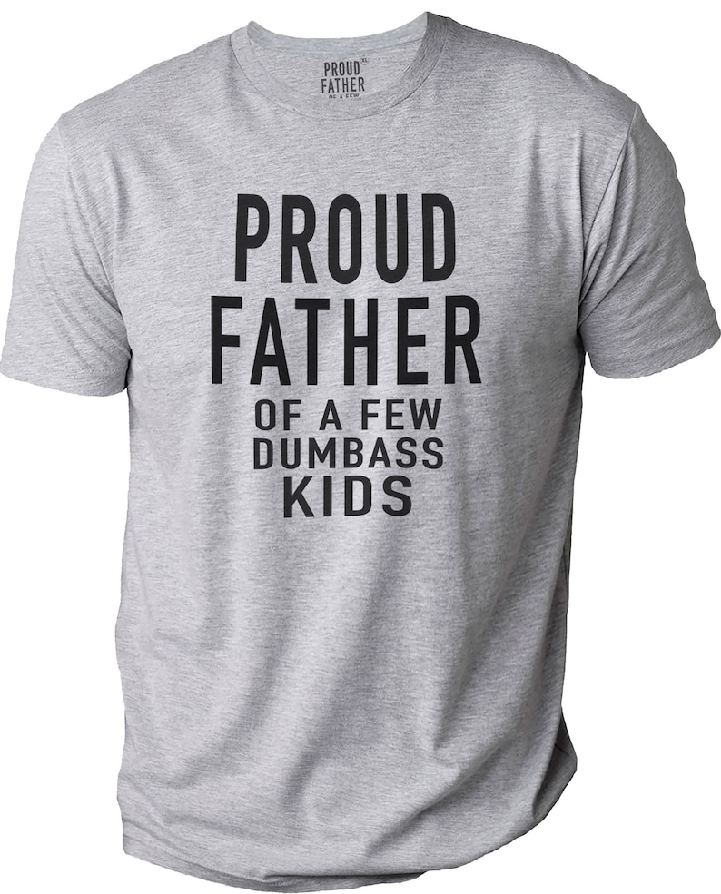 Puede incluir: Camiseta gris jaspeado con el texto "PROUD FATHER OF A FEW DUMBASS KIDS" en letras negras y negritas. La camiseta tiene cuello redondo y mangas cortas. La marca "PROUD FATHER" est&aacute; impresa en el cuello.