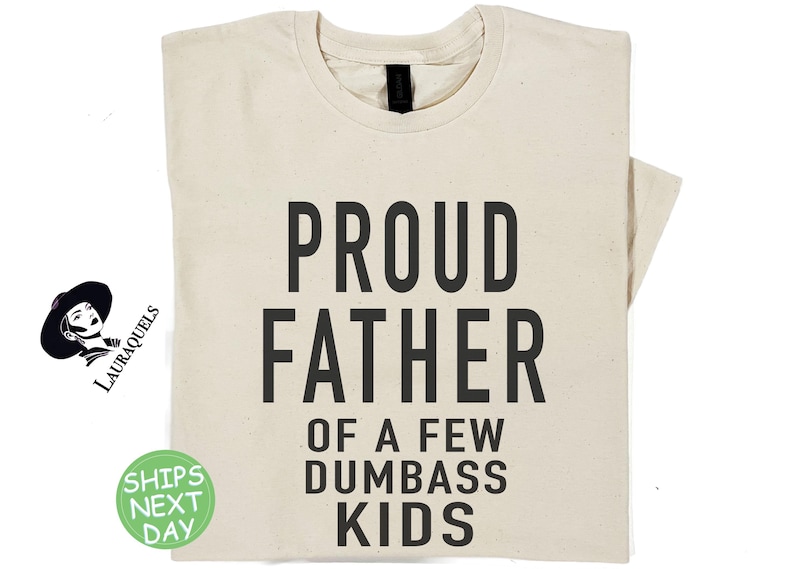 May include: A natural t-shirt with the text 'PROUD FATHER OF A FEW  DUMBASS KIDS' printed in black.