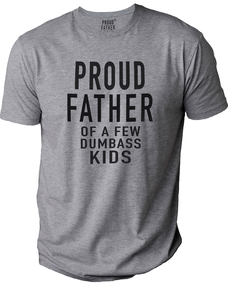 Puede incluir: Una camiseta gris jaspeada con el texto "PROUD FATHER OF A FEW DUMBASS KIDS" en letras negras en negrita. La camiseta tiene cuello redondo y mangas cortas. La marca "PROUD FATHER" est&aacute; impresa en el cuello.