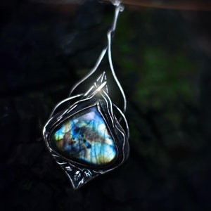 May include: A silver pendant with a blue and green labradorite gemstone set in a delicate wire design.
