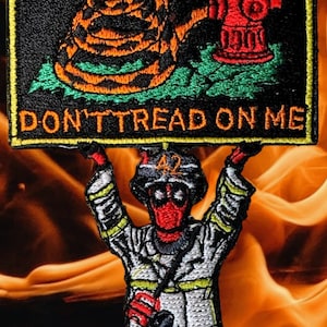 May include: A red and black firefighter figure holding a sign that says "Don't Tread On Me". The sign features a yellow snake coiled around a red fire hydrant on a black background.