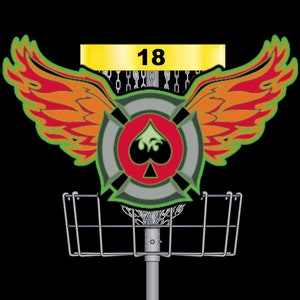 Könnte beinhalten: Ein Disc-Golf-Korb mit einem roten, grünen und schwarzen Ziel mit einem Pik-Symbol. Der Korb hat ein gelbes Banner mit der Nummer 18 darauf. Das Ziel hat Flügel mit orangefarbenen und roten Flammen.