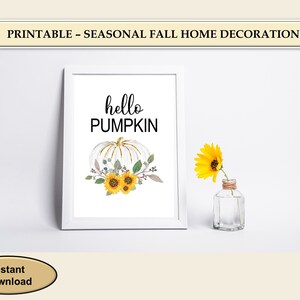 Könnte beinhalten: Druckbarer Wandkunst mit einem weißen Kürbis mit goldenen Akzenten und Sonnenblumen. Der Text "hello pumpkin" ist in Schwarz über dem Kürbis geschrieben.