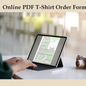 May include: A digital tablet displaying an "Online PDF T-Shirt Order Form" is positioned on a white surface. A vintage camera sits nearby. The form features a detailed layout with sections for order details and a t-shirt diagram.