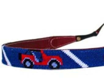 May include: Eyeglass holder with a blue and white striped pattern and a red jeep design. The holder has brown leather accents and is attached to a pair of round, dark sunglasses.
