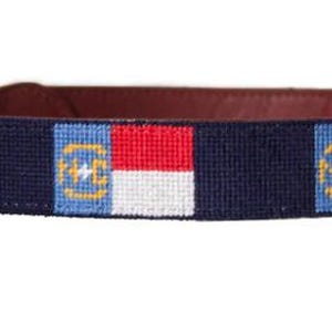 Puede incluir: Un collar de perro azul marino con una hebilla de cuero marr&oacute;n y un patr&oacute;n repetido de la bandera del estado de Carolina del Norte.