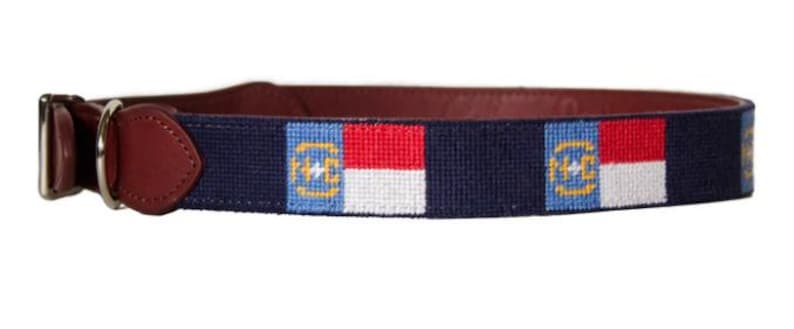 Puede incluir: Un collar de perro azul marino con una hebilla de cuero marr&oacute;n y un patr&oacute;n repetido de la bandera del estado de Carolina del Norte.
