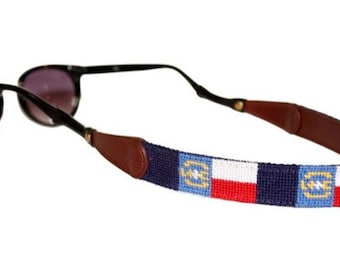May include: Sunglasses with a beaded strap featuring a Texas flag design. The strap is navy blue with white, red, and light blue accents. The sunglasses have black frames and dark lenses.