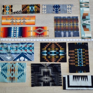 May include: A collection of eleven rectangular fabric swatches featuring various geometric patterns in colors including orange, blue, black, and white. A yellow measuring tape shows lengths up to 35 inches, providing scale for the assorted textile pieces.