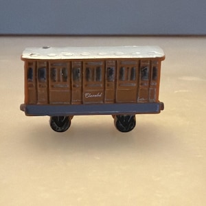 May include: A miniature brown train car with a silver roof and black wheels. The car has several rectangular windows and doors. The text "Clanabd" is visible on the side of the car. This toy train car is a collectible item.