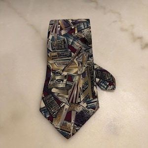 May include: A necktie featuring a dark purple background with a repeating pattern of drafting and engineering tools. The design includes illustrations of compasses, protractors, rulers, calculators, and computer monitors in shades of gold, blue, and grey.