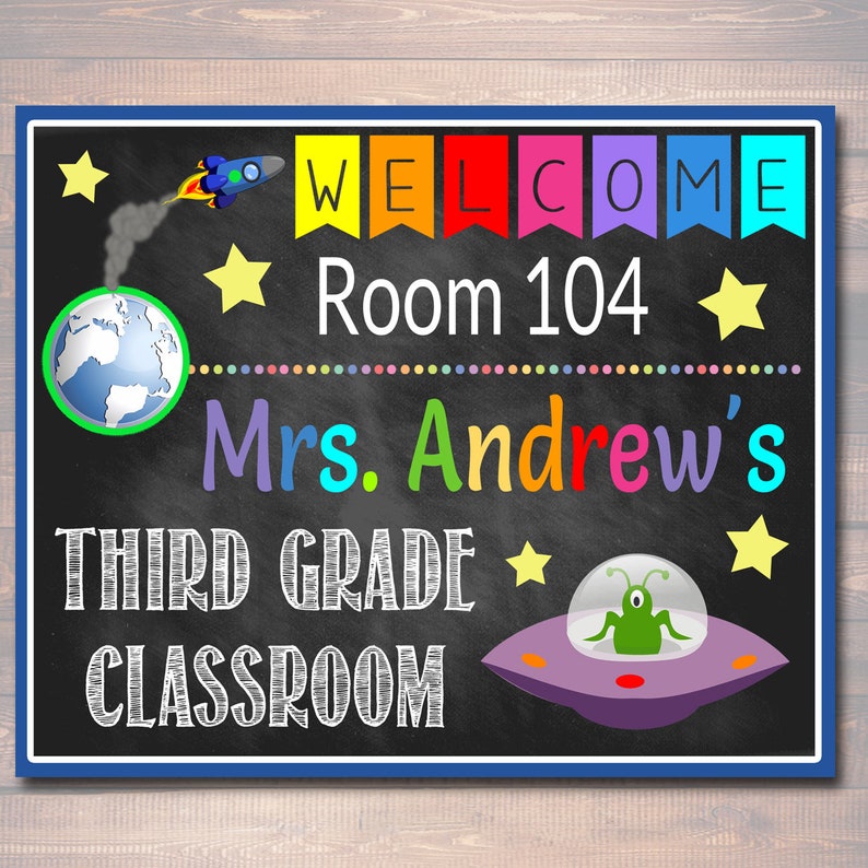 Puede incluir: Un cartel de bienvenida para el aula en una pizarra con tem&aacute;tica espacial. Dice "Bienvenido" en letras arco&iacute;ris, "Sala 104", "Clase de tercer grado de la Sra. Andrew", y presenta un cohete, estrellas, un planeta Tierra y un platillo volador con un extraterrestre.