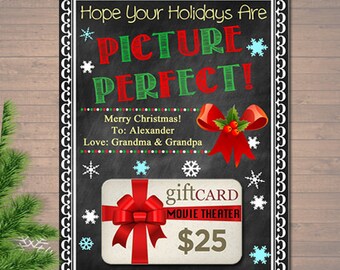 May include: A chalkboard style Christmas gift card with a red bow and the text "Hope Your Holidays Are Picture Perfect! Merry Christmas! To: Alexander Love: Grandma & Grandpa" and a gift card for a movie theater for $25.