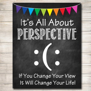 May include: Black chalkboard with a rainbow banner at the top. The text "It's All About PERSPECTIVE" is written in white chalk. A white upside-down smiley face is drawn below the text. The text "If You Change Your View It Will Change Your Life!" is written in white chalk at the bottom.