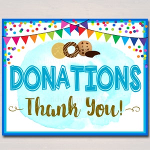 May include: A blue and white sign with the text "DONATIONS Thank You!" in brown text. The sign is decorated with colorful confetti and a string of flags. There are three cookies on the sign: a chocolate chip cookie, a donut, and a shortbread cookie.