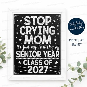 May include: A rectangular white frame containing a black chalkboard-style sign with white text that reads: STOP CRYING MOM it's just my First Day of SENIOR YEAR CLASS OF 2027. The sign includes star accents and is sized at 8x10 inches.