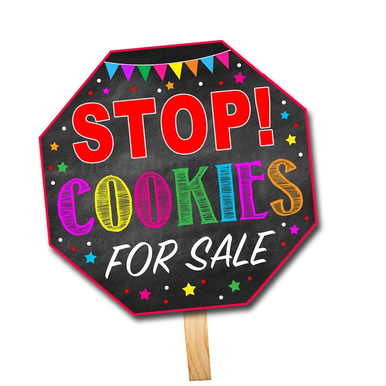 May include: A red octagon-shaped sign with the words "STOP! COOKIES FOR SALE" written in colorful letters on a black chalkboard background. The sign is decorated with colorful stars and a string of flags.