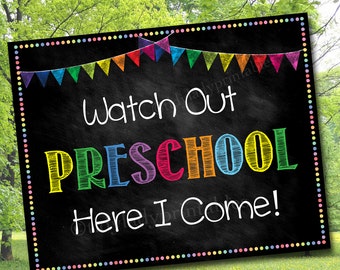 May include: A black chalkboard sign with a colorful rainbow banner at the top. The sign says "Watch Out Preschool Here I Come!" in white text with a colorful rainbow outline.