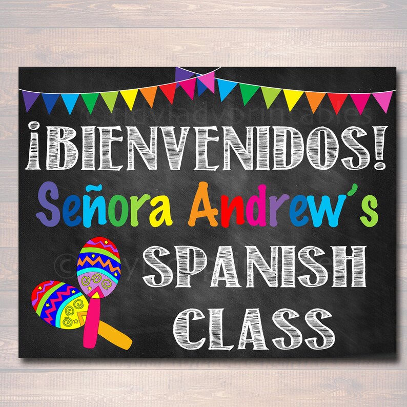May include: A black chalkboard sign with colorful pennant flags at the top. The sign says "&iexcl;BIENVENIDOS! Se&ntilde;ora Andrew's SPANISH CLASS" in white chalk. There are two colorful maracas on the left side of the sign.