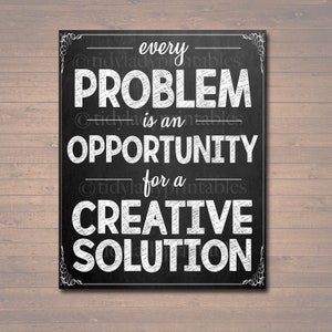 May include: A black chalkboard-style print with white text that reads "every PROBLEM is an OPPORTUNITY for a CREATIVE SOLUTION." The print has a decorative white border and is set against a wooden background.