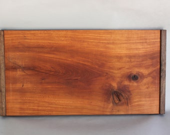 Könnte beinhalten: Ein rechteckiges Holztablett mit einer natürlichen Holzoptik und dunkelbraunen Holzverzierungen. Das Tablett hat ein rustikales Aussehen mit sichtbaren Knoten und Maserungen im Holz.