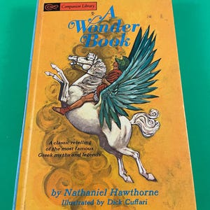 May include: A yellow book cover with a white winged horse and a rider. The title is "A Wonder Book" and the book is by Nathaniel Hawthorne, illustrated by Dick Cuffari. The book is a classic retelling of Greek myths and legends.