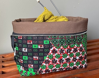 May include: A brown canvas zippered pouch with a black and green patterned fabric lining. The pouch is filled with yellow yarn and knitting needles.
