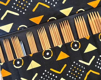 May include: A black fabric roll-up case featuring a yellow and white geometric pattern, containing multiple sets of wooden knitting needles and one pair of silver-toned metal needles organized in individual vertical slots.