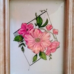 以下が含まれることがあります： 幾何学模様の中にピンクの花が描かれた額縁付きの絵。花は繊細なディテールで写実的に描かれている。額縁は明るい木の色です。