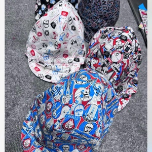 May include: Four Star Wars themed baseball caps. The caps are made of cotton fabric and feature different designs. One cap is white with red and blue Star Wars characters, another is blue with red and white Star Wars characters, another is black with white Star Wars characters, and the last is black with blue and white Star Wars characters.