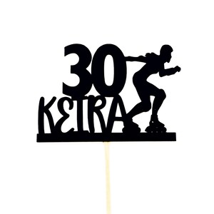May include: Black silhouette of a person roller skating with the number 30 and the word "KEIRA" in front of them. The silhouette is on a cake topper.
