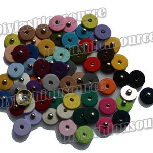 May include: A collection of colorful, round fabric-covered snaps in various shades, including pink, blue, yellow, and green. Each snap has a silver metal center. The image is taken from a high angle.