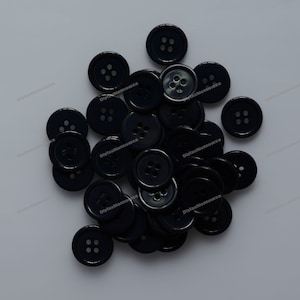 Può includere: Un mucchio di bottoni di plastica neri con quattro fori ciascuno. I bottoni sono disposti in modo casuale.