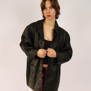 May include: A black leather jacket with a button-up front, worn over a black top and a colorful, patterned skirt. The skirt features a vibrant mix of red, pink, and orange vertical stripes. Black heeled sandals complete the outfit.