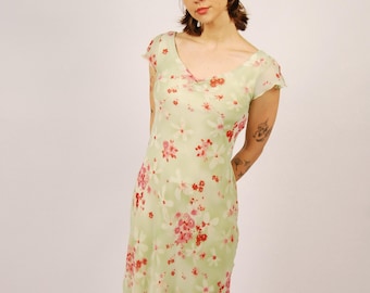 May include: A light green dress with a floral pattern in pink and red. The dress has a scoop neckline and cap sleeves. The hem is ruffled. The model is wearing brown sandals. The dress is knee-length.