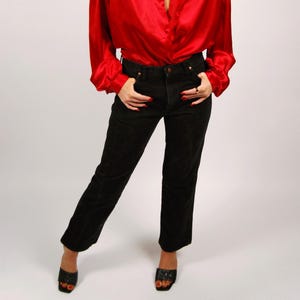 May include: A red satin blouse with long sleeves and a collared neckline paired with black denim jeans. The outfit is completed with black open-toe heels. The model is wearing pink-tinted sunglasses.